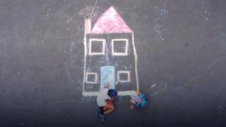 An ariel view of two children drawing a house using chalk.