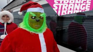 A Grinch in a Santa costume and the Strange logo