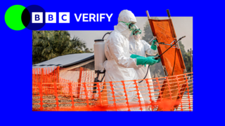 Two medical workers in protective clothing spraying down an orange stretcher amid Ebola outbreak.