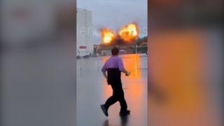 A man is seen in the foreground, behind him is a large explosion