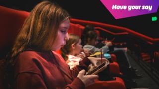 Teenager sitting the cinema looking at her phone