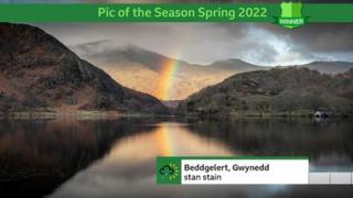 Pic of the season winner shows a rainbow between two craggy mountains and reflected in the water below.