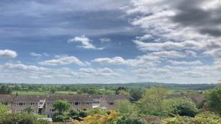 Blue skies and light white clouds over a view of houses and countryside.