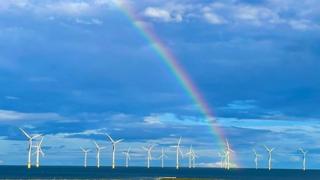 A rainbow rises into a very blue cloudy sky over a stretch of sea covered in wind turbines