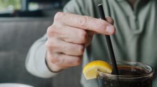 A man holding a straw standing in a glass of pop.