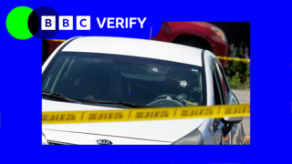 A white car with bullet holes through the window, surrounded by police tape. There is blue and green BBC Verify branding in the top left corner.