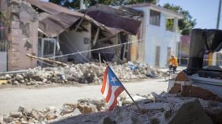 A Puerto Rican flag stands amoungst earthquake debris