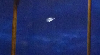 A grainy image shows a classic "flying saucer" set against a dark blue sky.