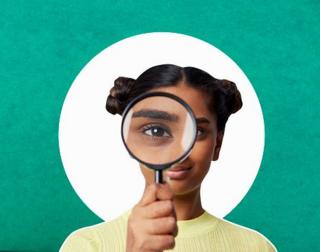 young woman looking at camera with magnifying glass with green background
