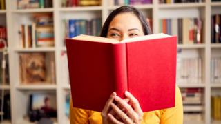A woman peeps over a book in a library