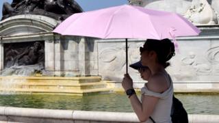 People shelter under an umbrella from the scorching sun next to the Victoria Memorial outside Buckingham Palace in London