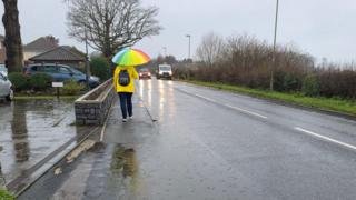 Person walking along pavements with localised flooding on the road and pavement following Tuesday's rain.
