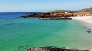 Green and blue seas in a cove in Clachtoll, Highland, with blue sky above