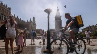 Man on a bicycle near in a square in Poland with the sunshine beating down.