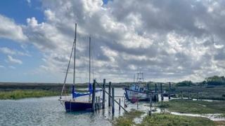 Two boats sit in a river with a backdrop of cloudy blue skies