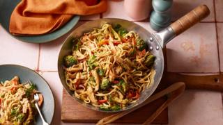 A wok containing a large portion of peanut noodles with broccoli and chicken