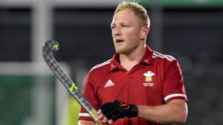 Rupert Shipperley in red Wales shirt wearing cloves and holding a hockey stick