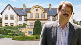 The entrance to a mansion. The property is a beige and white colour with perfectly trimmed bushes in front of the house. A circular driveway can be seen looping around the entrance to the property. And there is also a photoshopped image of Danny Dyer on the image.