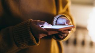 A person in a yellow jumper uses a smartphone.