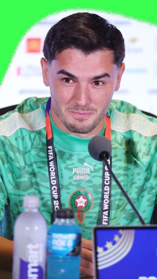 Brahim Diaz smiling at a press conference. He is wearing a green Morocco training kit.