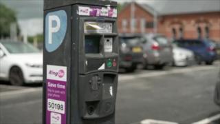 A black pay and display machine with cars parked behind.