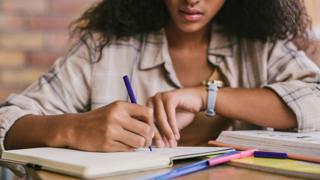 student writing in a book in a classroom - stock image