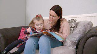 A mum and her daughter looking at a picture book together.