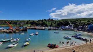 A bright blue sky over a bay in Stonehaven. People are on the beach and in the water going out in boats.