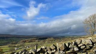 Blue skies with white clouds over Cumbrian fields with a stone wall in the foreground