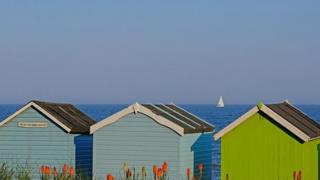 The rear of three coloured beach huts in Felixstowe, Suffolk, with the blue sea and lighter blue sky behind.