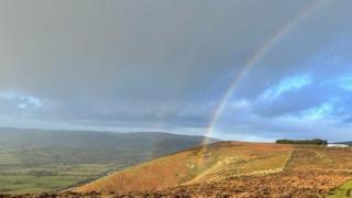 A double rainbow over an auburn and green hillside.