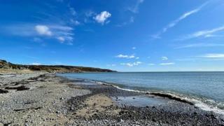 Blue skies with a few wispy clouds next to a sandy shoreline.