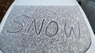 'Snow' written in light snow on a car windscreen