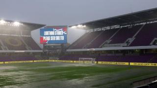 view of a stadium with heavy rain flooding part of the pitch. The big sign says lightning strikes, please seek shelter