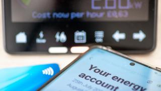 Energy account on phone next to bank card and in front of smart meter reading.