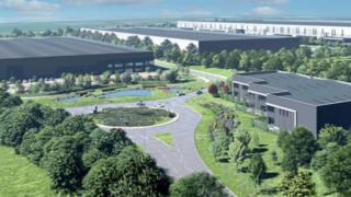 An artist's impression of what a number of warehouses could look like, including several grey buildings, a roundabout, roads, trees, grass areas, and bushes.