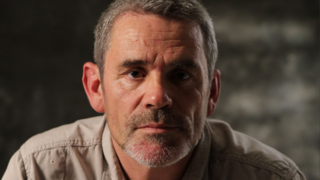 Paul Conroy poses for a headshot. He has short greying hair and stubble.