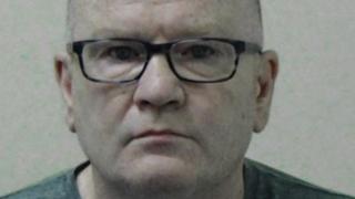 Mugshot of Campbell. He is bald and clean shaven and is wearing black-framed glasses.