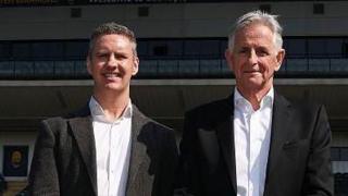 Stephen Vaughan stands next to Worcester Warriors owner Chris Holland in font of the main stand at Sixways. Both are wearing dark suits with white shirts and have their hands crossed in front of their waists.