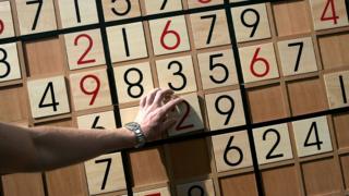 Person completing sudoku puzzle on a wooden board