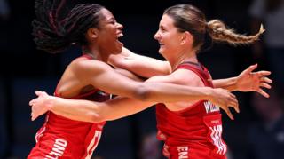 Fran Williams and Olivia Tchine, wearing England's red netball jersey, celebrate after beating South Africa to reach the semi-final by jumping in the air and hugging each other