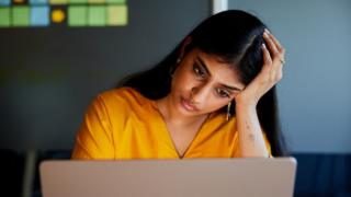Stock shot of a woman in an orange top at a computer. She looks concerned.