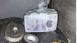 A plastic bag containing a stack of £20 notes alongside some tape.
