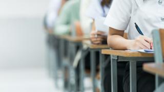 Students Taking Exam in Classroom Setting. Students in uniforms are seated in a classroom, writing answers during an exam, highlighting focus and academic testing. - stock photo