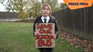 ella holding a sign that reads "save our school bus"