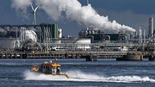 An oil refinery at the Port of Rotterdam. In the foreground a small boat leaves a wake in the water.