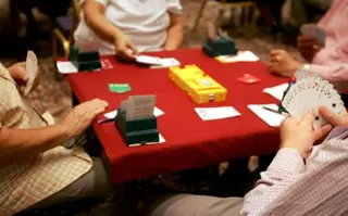 A red table with playing cards - 4 people sit around the table playing Bridge.