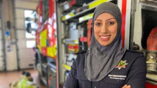Photograph of Uroosa, a firefighter, standing next to a fire engine.