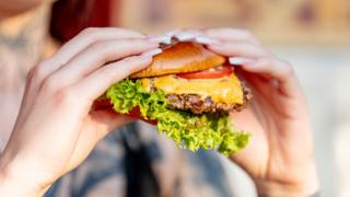 Woman holds freshly made cheeseburger outdoors in the summer sun. - stock photo