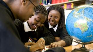 Three GCSE students in a school classroom work on a geography project with a globe on the table.